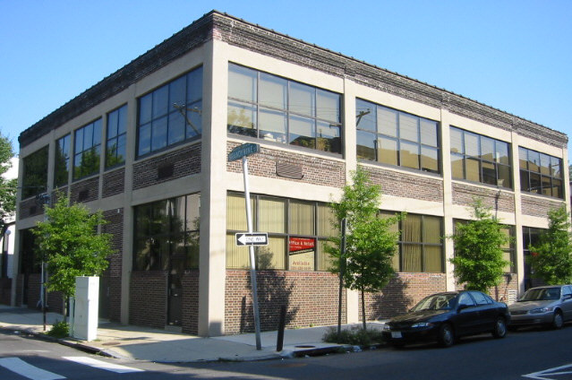 Photograph of TALtech's Philadelphia-based office building on a sunny day. The building is a two-story building with a warehouse look and large windows.